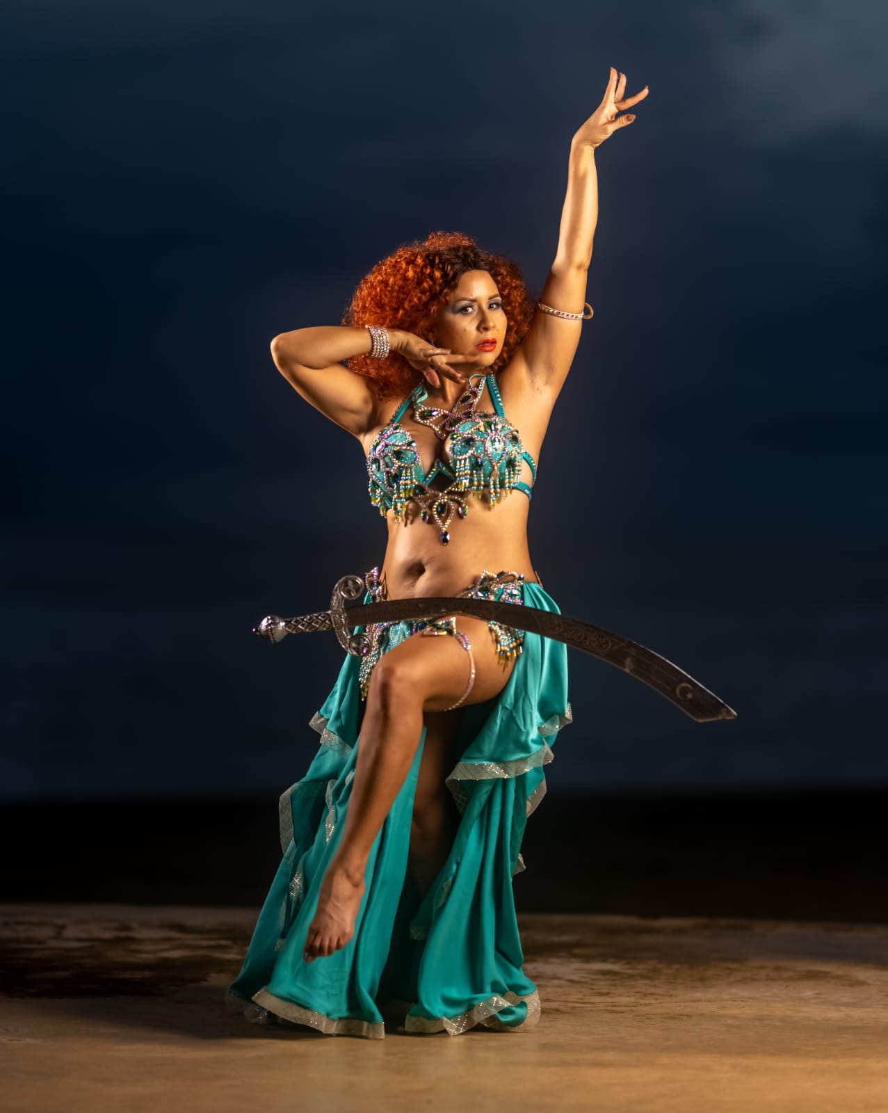 Adira Yamilet equilibrando una espada sobre la cadera con un traje turquesa de belly dance.